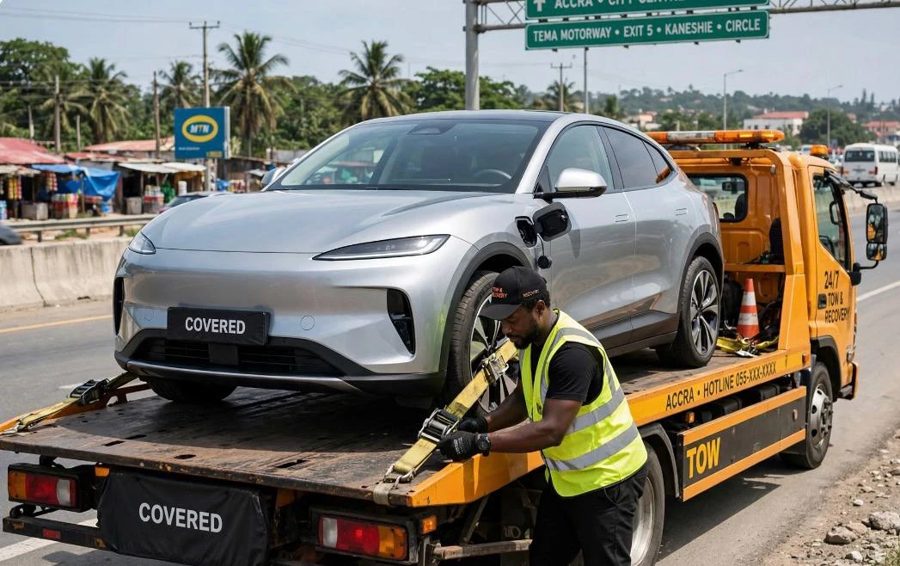 A tow operator strapping a silver electric SUV onto an orange flatbed truck