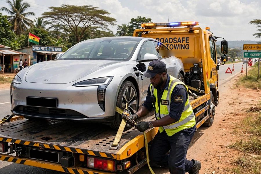 A tow operator strapping a silver electric car onto a flatbed truck