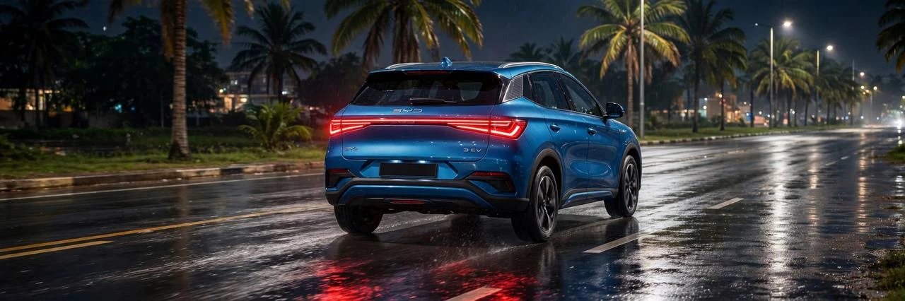 A blue electric SUV driving down a wet palm-lined road at night